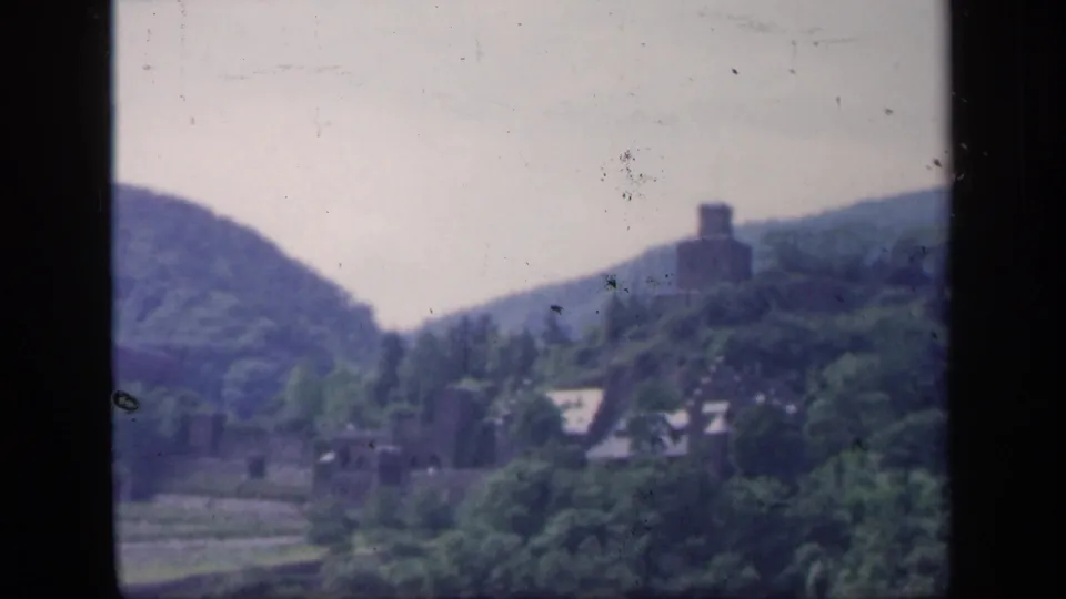 1949 Ireland 8mm frame showing a distant ruin above trees, with valley land and dark scan borders visible.