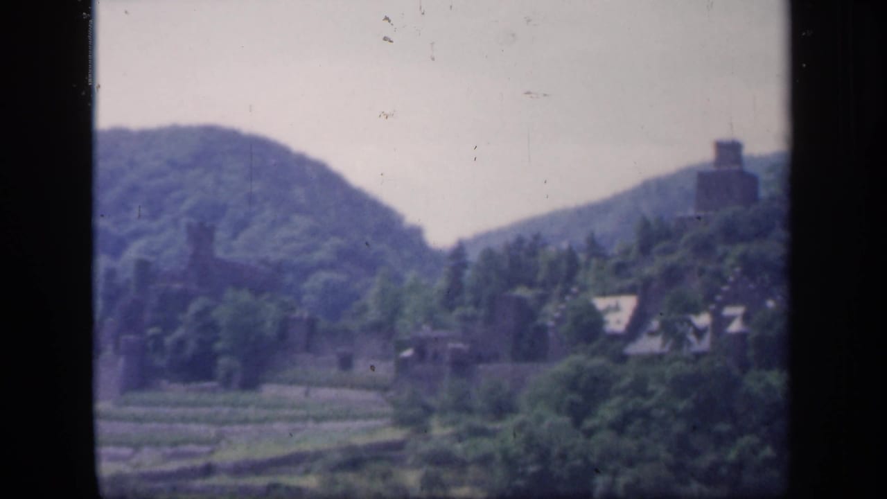 Distant tower on a wooded hill above fields and rooftops.