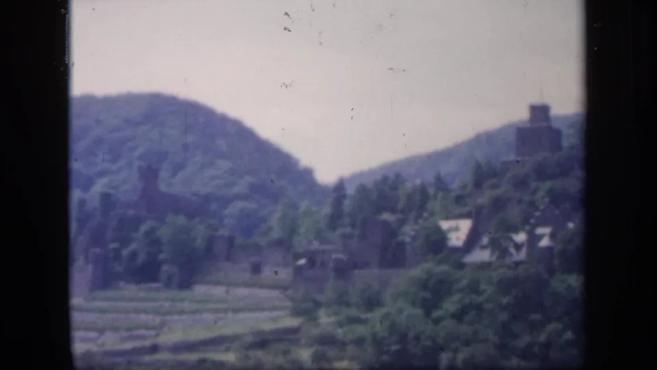 1949 Ireland 8mm frame with a tower-like building on a hillside above green fields, trees, and valley buildings.