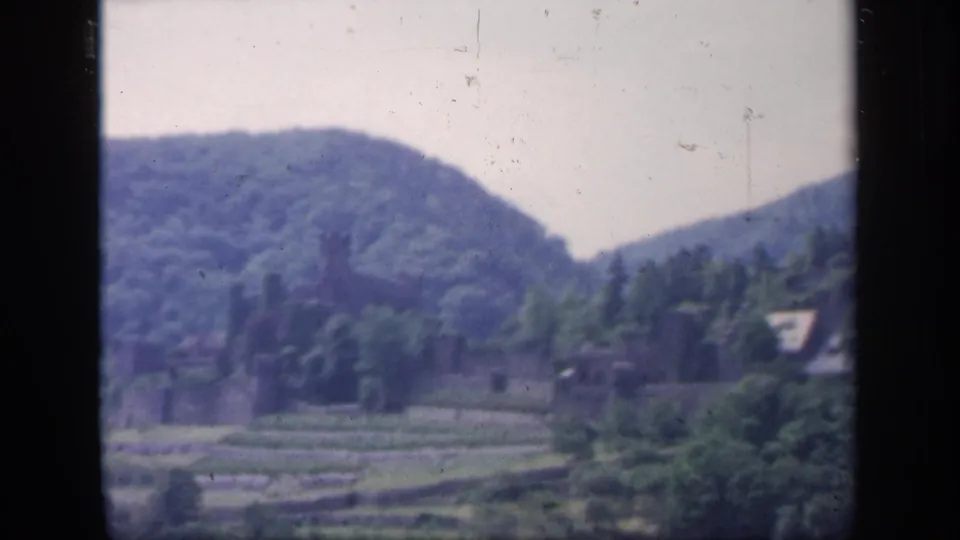 1949 Ireland 8mm frame showing a soft-focus view of wooded hills, terraced fields, and stone buildings in a rural valley.