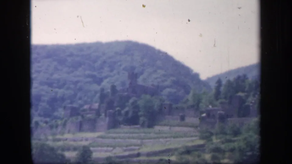 1949 Ireland 8mm frame with a wooded mountain slope, valley fields, and a distant stone ruin-like structure.