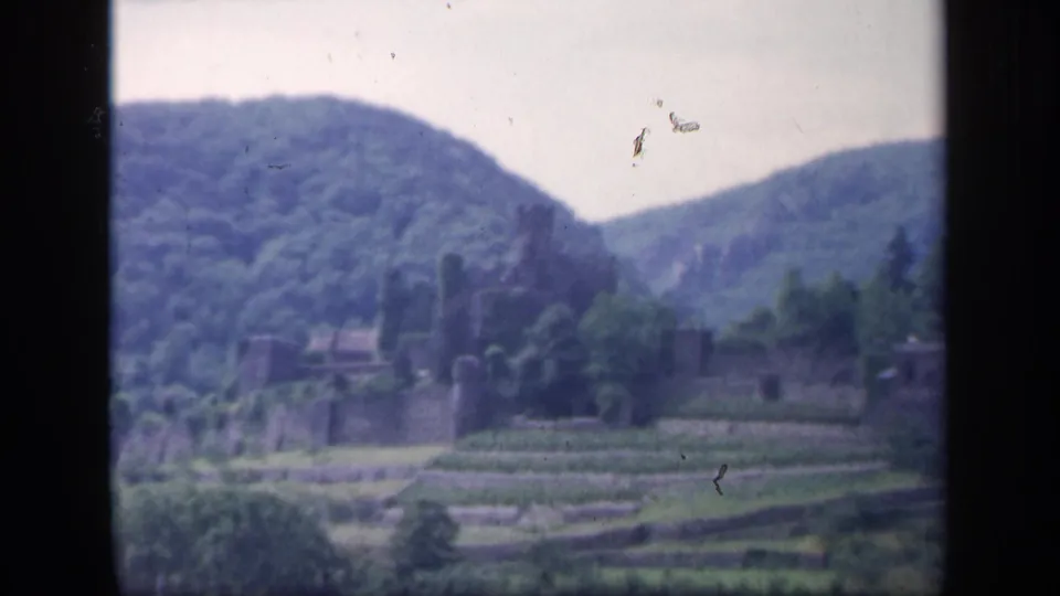 Distant 1949 Irish home-movie view of castle ruins, terraced fields, and blue-green hills with visible dust specks.