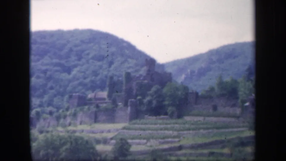 1949 Ireland 8mm frame of a rural castle landscape with terraced fields, stone structures, and wooded hills.