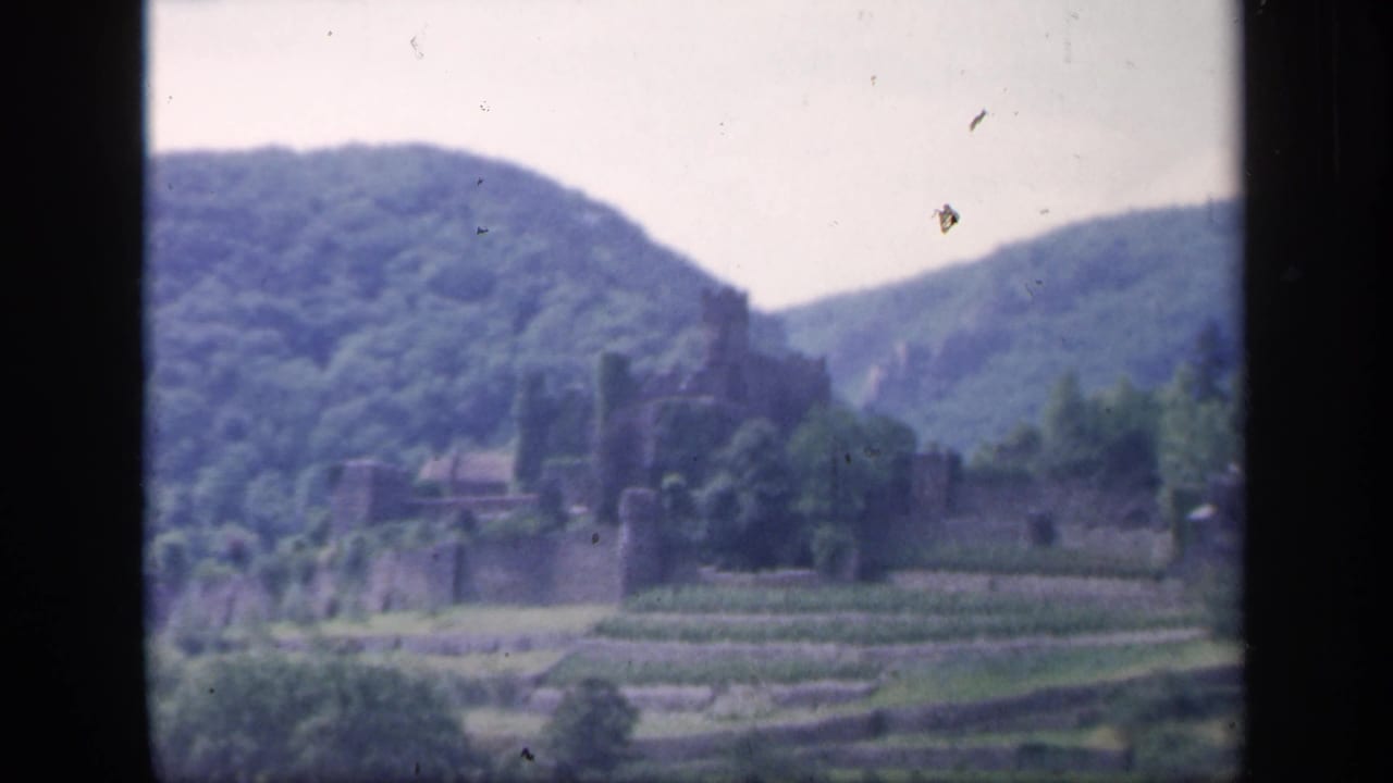 1949 Ireland 8mm frame showing distant stone castle ruins, terraced fields, trees, and green hills.