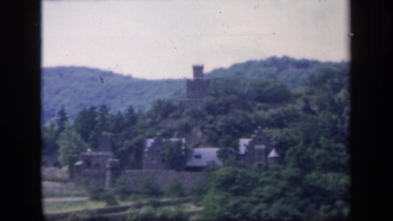 1949 Ireland 8mm frame with a square stone tower on a wooded hillside above smaller stone structures.