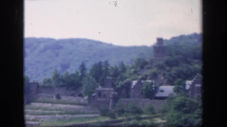 1949 Ireland 8mm frame looking across trees and fields toward a distant stone tower on the hillside.