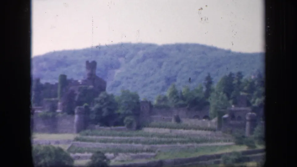Soft 8mm frame of castle ruins in Ireland, partly screened by trees with terraced rows and wooded hills behind.