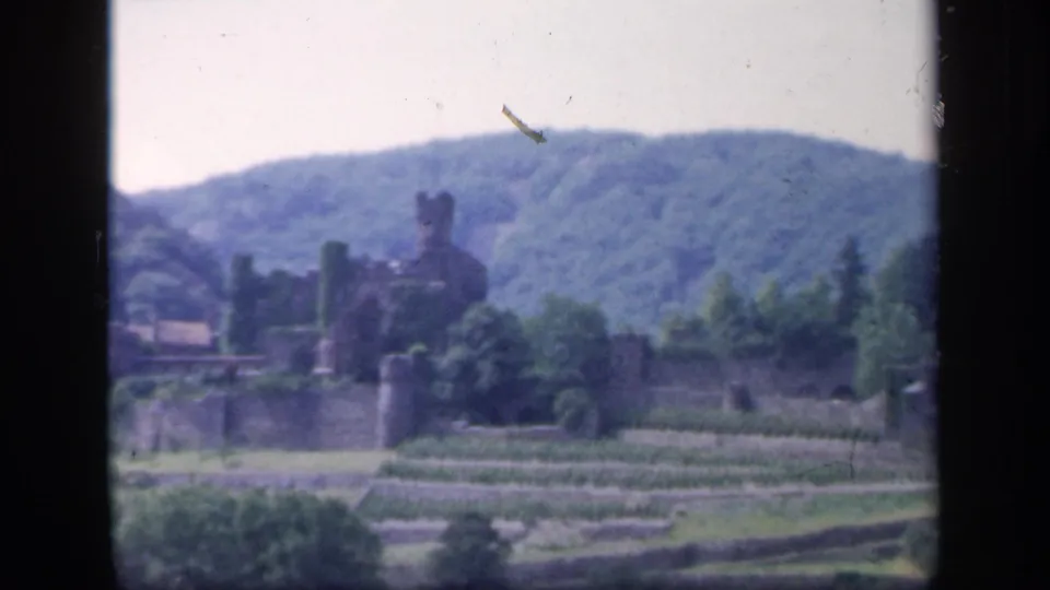 Ireland castle ruins are seen from a distance with stone walls, terraced grounds, trees, and wooded hills in faded 8mm color.