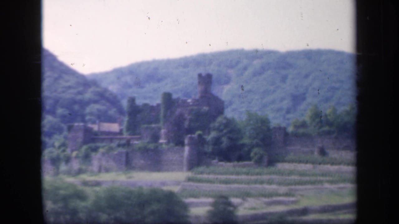 Distant stone castle set against green hills with terraced grounds in front.