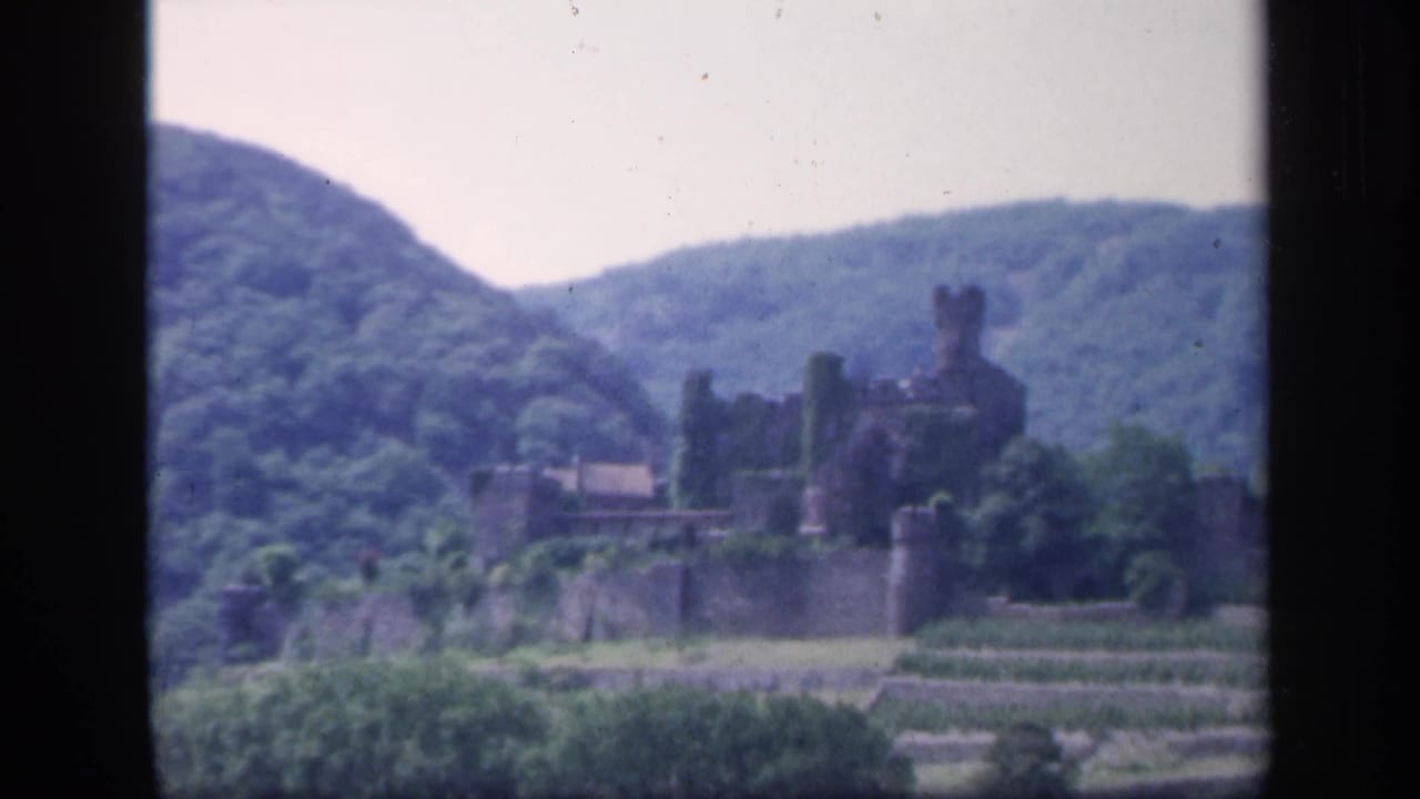 Distant castle and stone walls framed by green hills and pale sky.