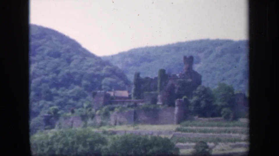 1949 Ireland travel footage frame with a castle-like stone structure, walls, terraces, and forested hills in soft 8mm color.