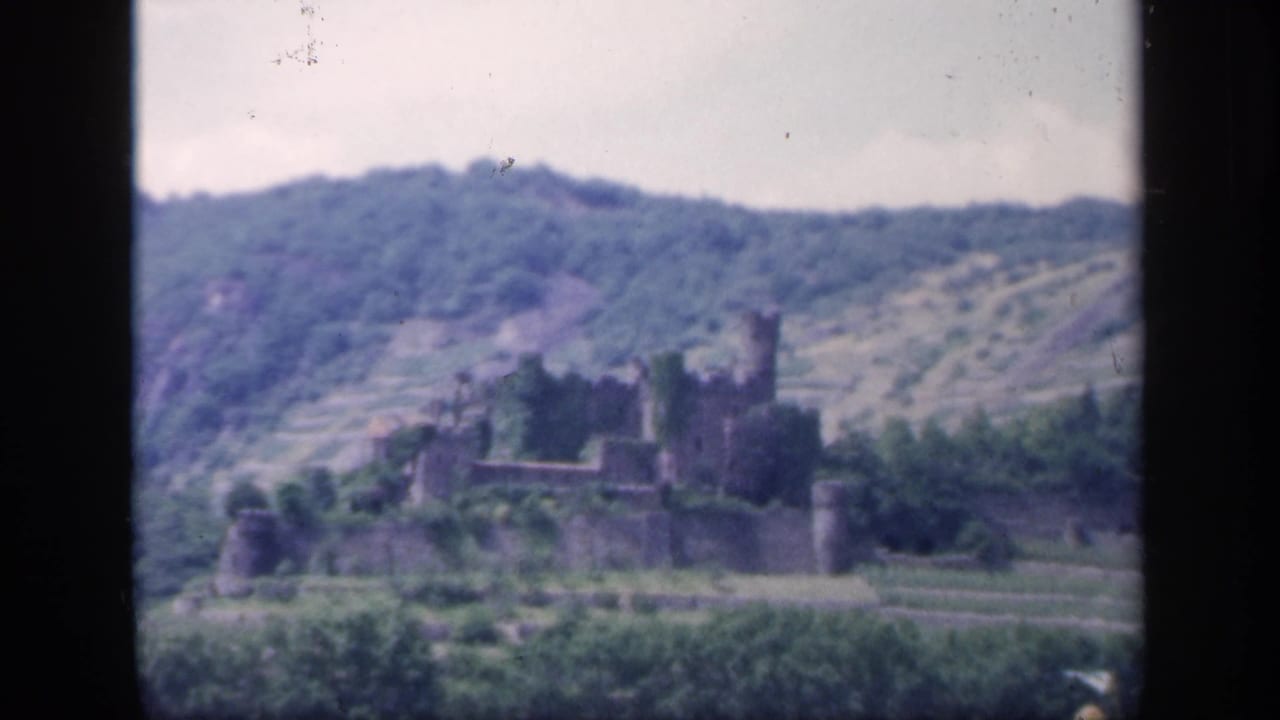 Distant stone castle ruin on a green hillside with dark 8mm frame borders.