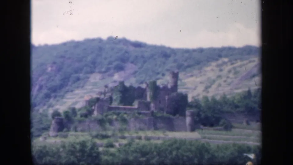 1949 Ireland 8mm frame showing a distant castle ruin set against a wooded green hillside and terraced slopes.