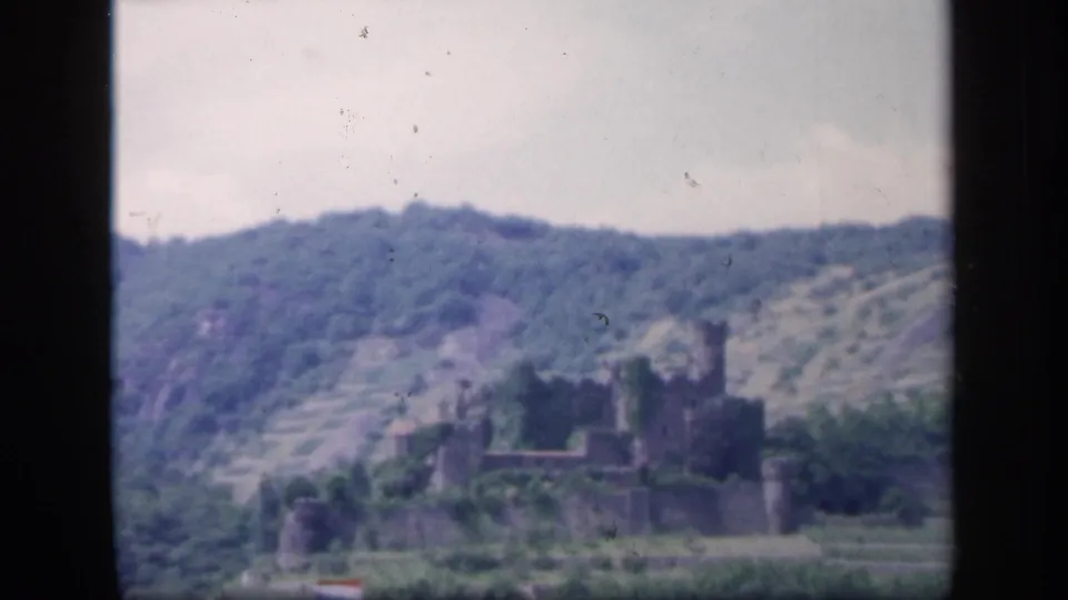 1949 Ireland 8mm view of a castle ruin below a wooded ridge, with soft focus and visible film dust.