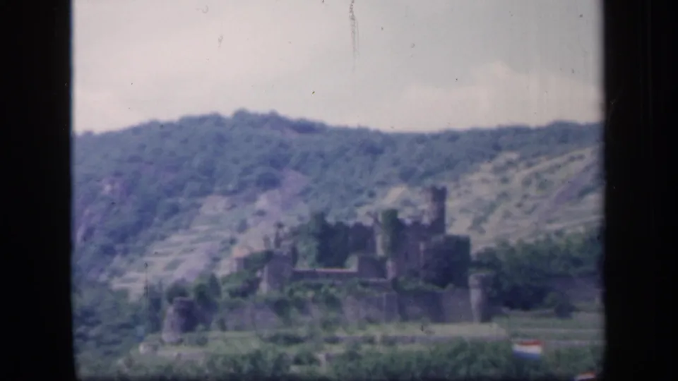 1949 Ireland home-movie frame with a distant castle ruin, terraced hillside, trees, and soft 8mm color.