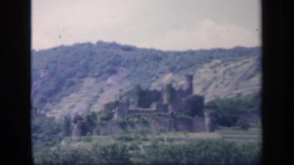 1949 Ireland 8mm frame showing a castle ruin across a valley, with green vegetation and a hazy hillside behind it.