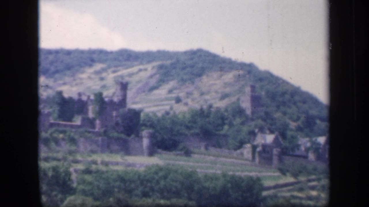 Stone ruin and tower on a wooded hillside with terraces and a pale sky.
