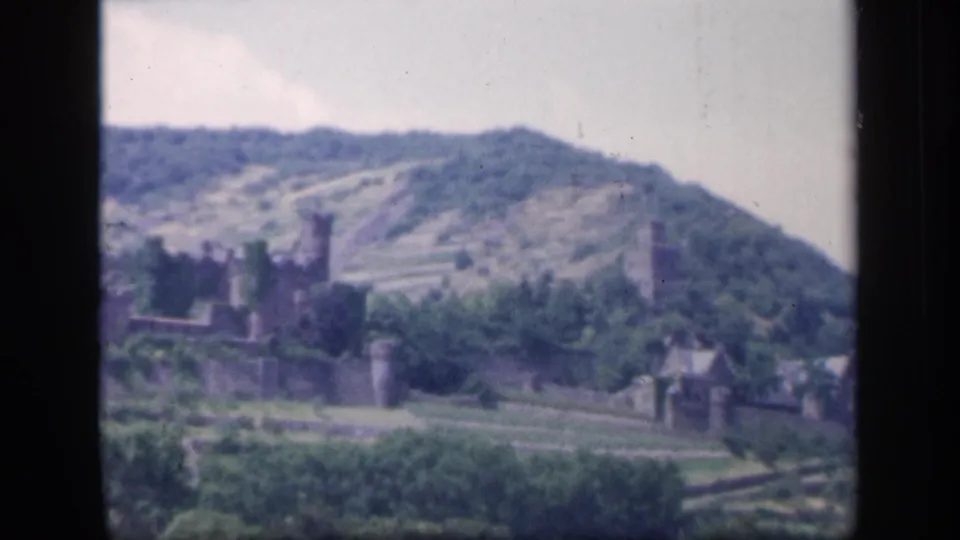 1949 Ireland home-movie frame of a stone ruin and tower set against wooded terraced hillsides.