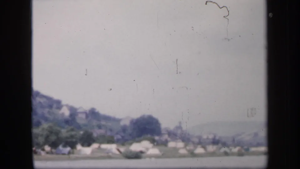 Soft 1949 Ireland 8mm frame showing tents, trees, water, and distant hillside settlement forms.