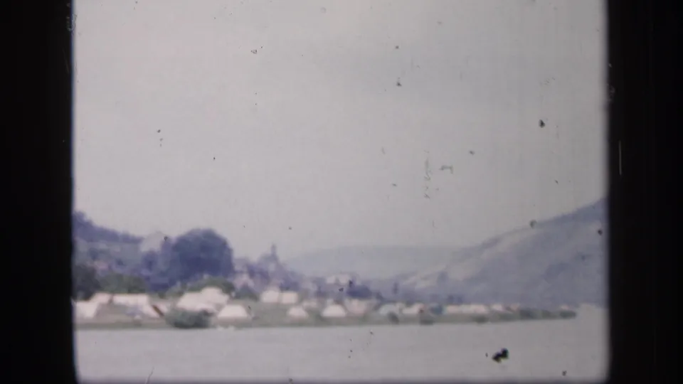 1949 Ireland 8mm frame of a quiet riverside campsite, with tents and trees set against hazy hills.
