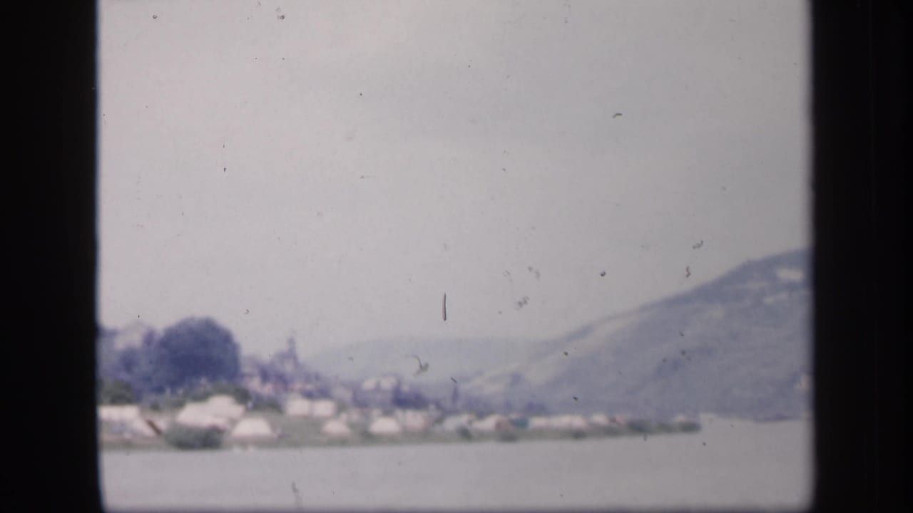Distant shoreline with pale structures beneath a hazy mountain across water.