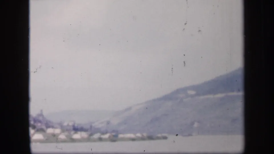 1949 Ireland home-movie frame with small pale shoreline forms and a broad, mist-softened mountain beyond the water.