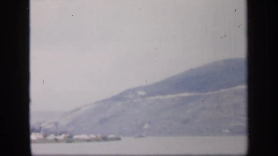 1949 Ireland 8mm frame centered on a hazy mountain slope above water, with a partial shoreline at the lower edge.