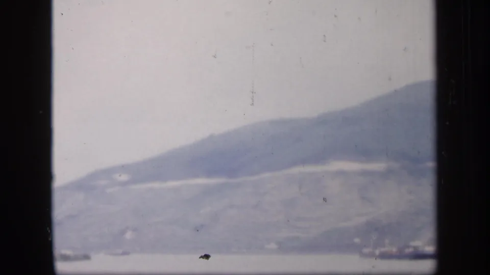 1949 Ireland home-movie frame showing a broad misty mountain above calm water, with faint shoreline detail near the frame edge.