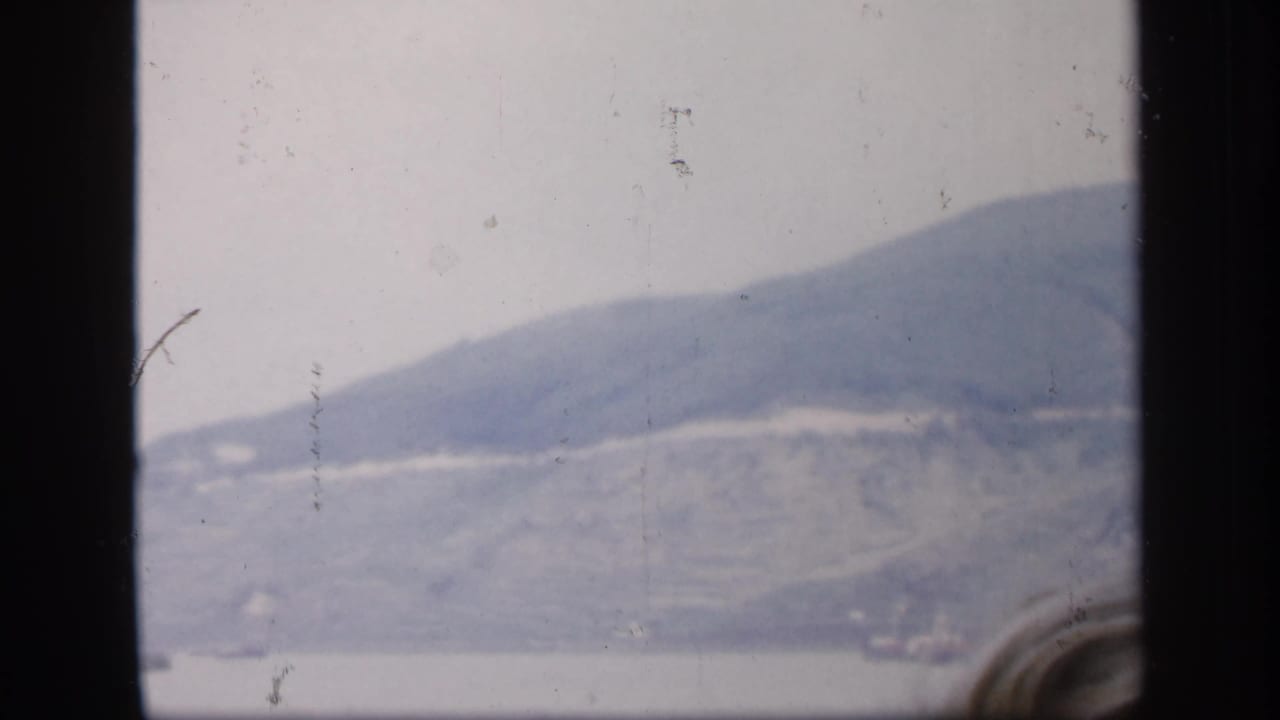 Misty shoreline and hillside seen through dark vertical window edges.