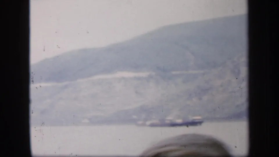Soft 1949 Ireland travel frame with water, hillside, and a possible distant boat seen past dark frame edges.