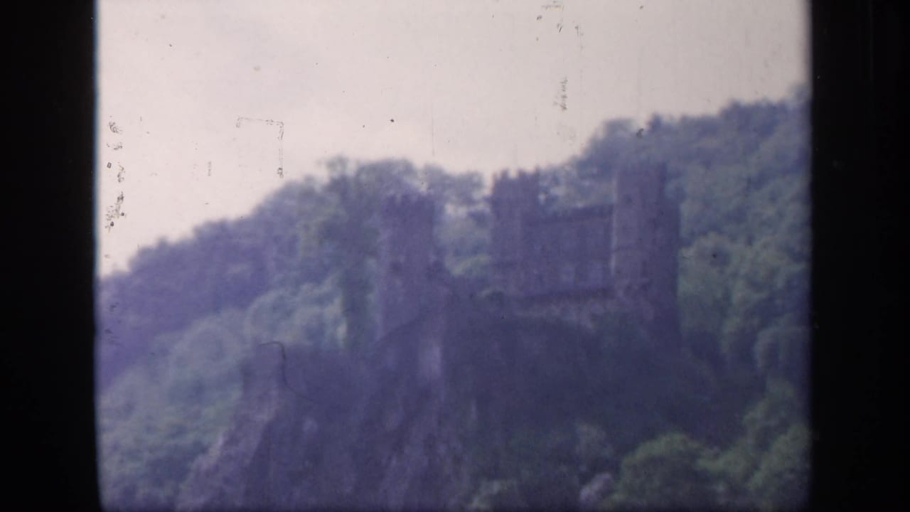 1949 8mm Ireland view of a dark stone castle-like ruin rising from a wooded hillside in soft focus.