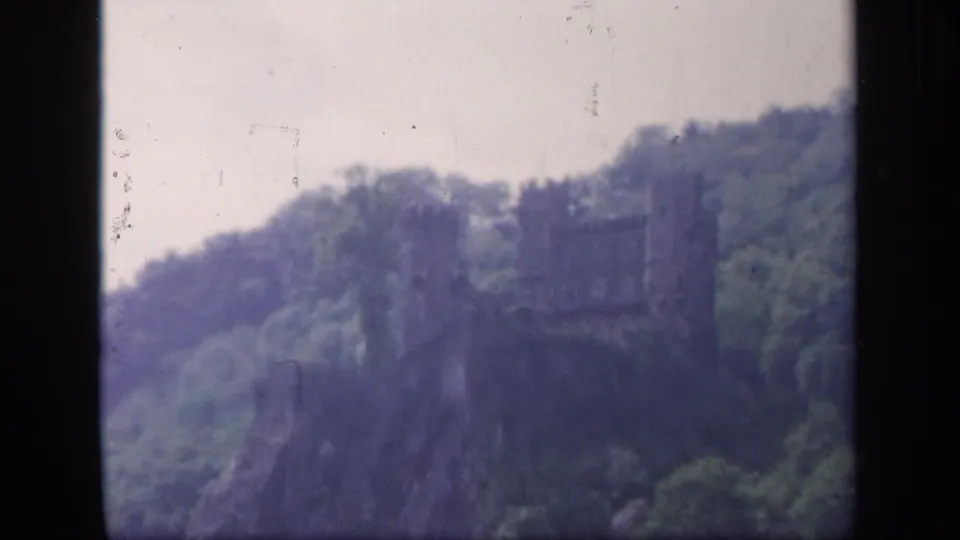 1949 8mm Ireland view of a dark stone castle-like ruin rising from a wooded hillside in soft focus.