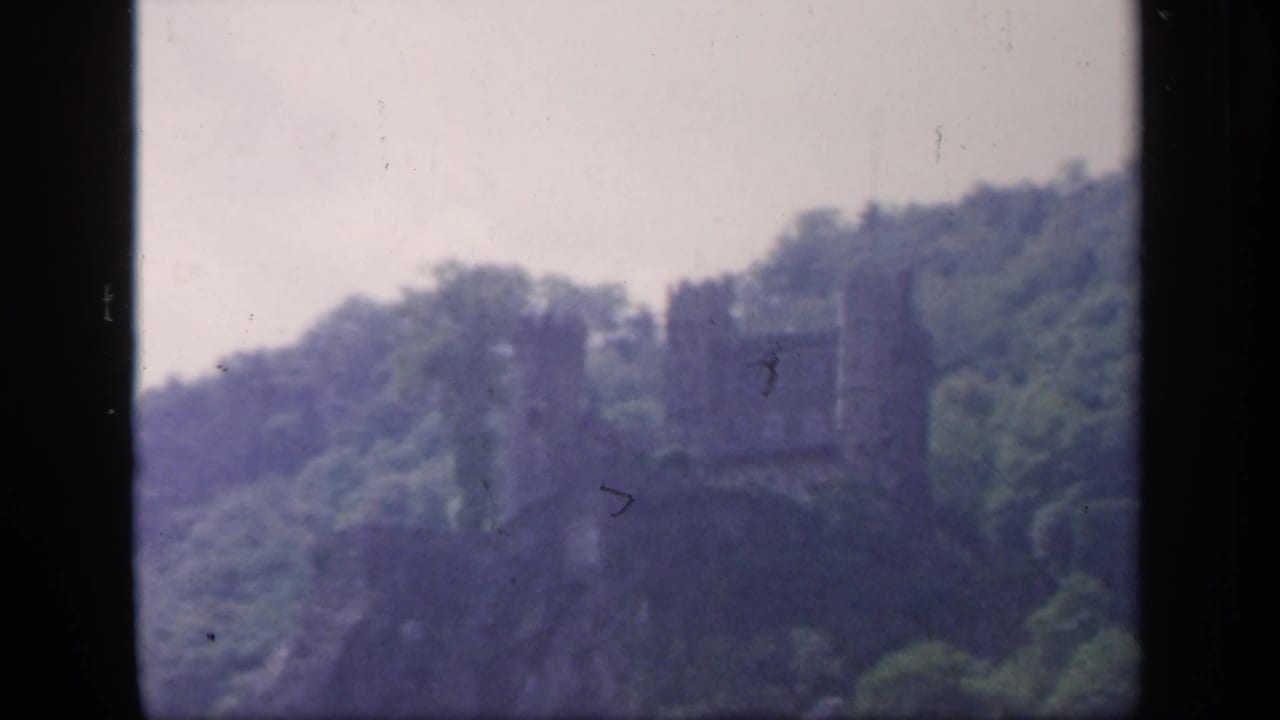 A distant castle-like ruin on an Irish wooded hillside, seen in faded 1949 8mm home-movie color.