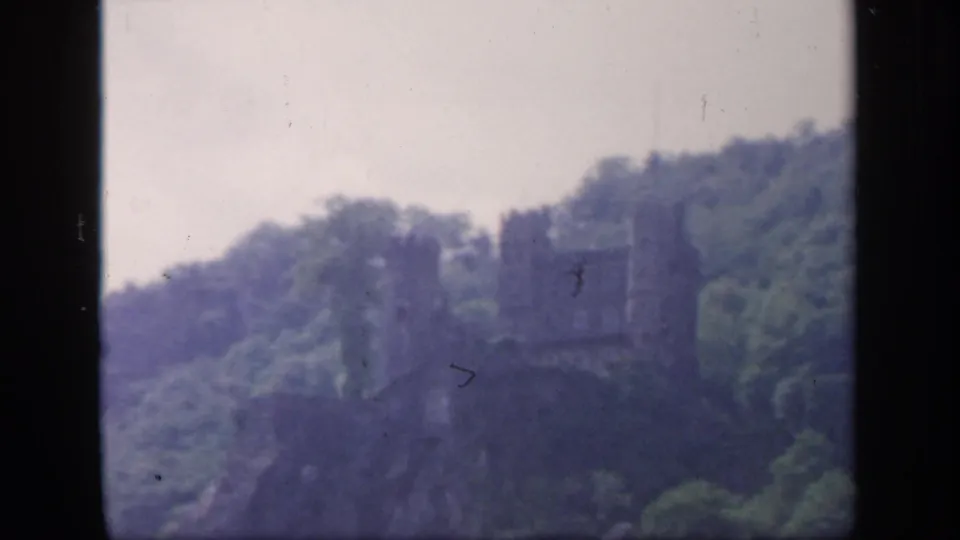 A distant castle-like ruin on an Irish wooded hillside, seen in faded 1949 8mm home-movie color.