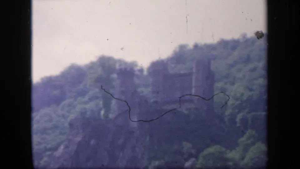 1949 Ireland home-movie frame with a hilltop stone ruin, wooded slope, pale sky, and visible 8mm surface marks.