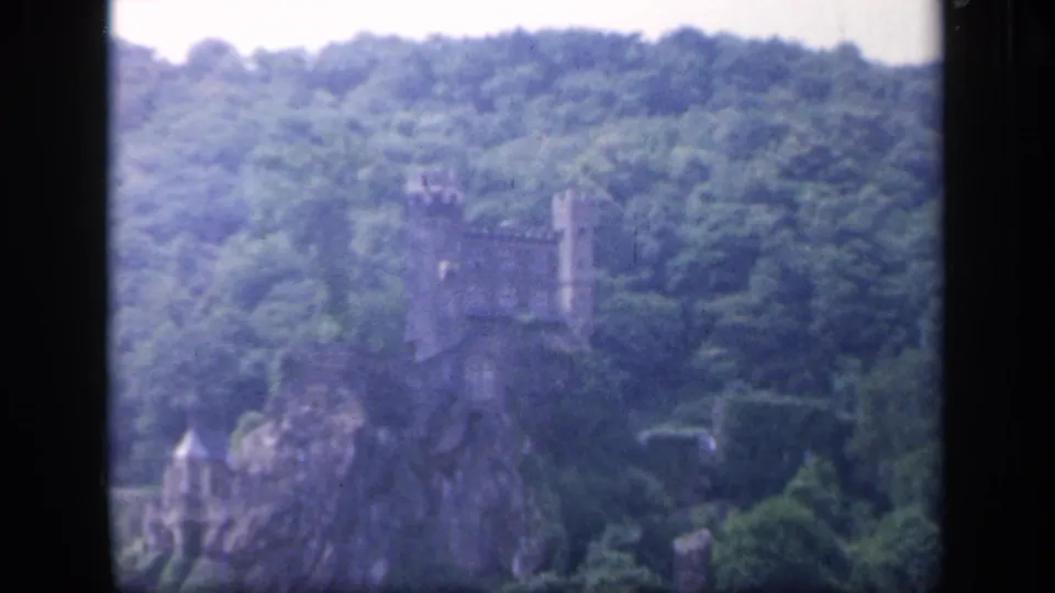Wider 1949 8mm Ireland view of a castle-like ruin on a rocky, tree-covered hill with a smaller tower below.