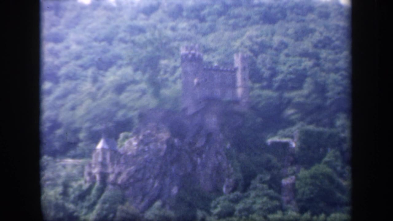 Castle tower and smaller turret visible above rocks and dense trees.