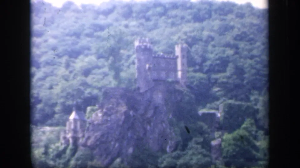 Soft 1949 Ireland 8mm frame showing a castle on a rocky outcrop, surrounded by green trees and dark film borders.