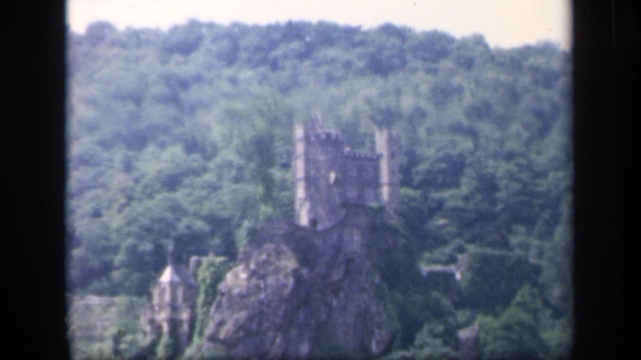 Distant castle on a rocky wooded outcrop seen across a river.