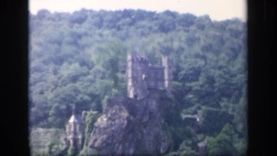1949 8mm Ireland footage shows a distant stone castle above trees on a rocky outcrop, viewed from across water.