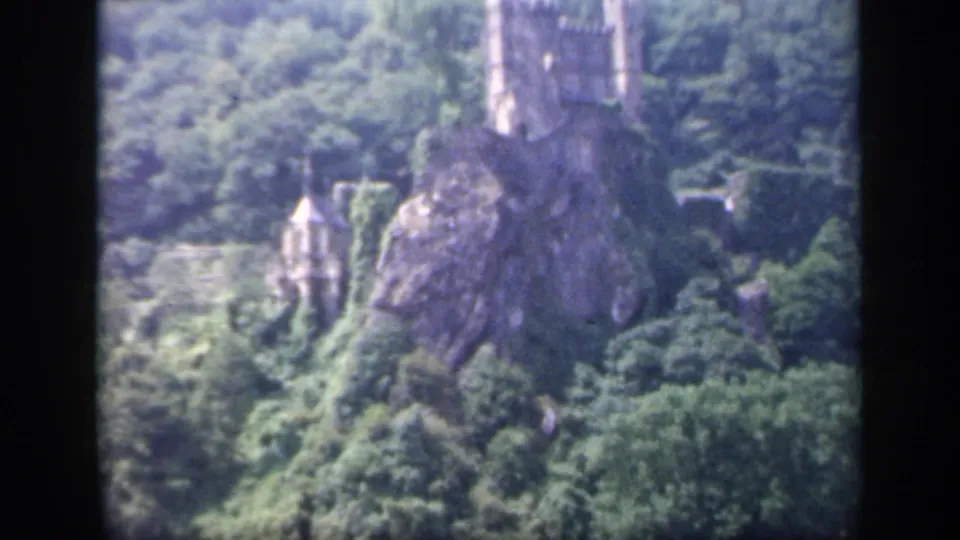 Soft 8mm frame from Ireland in 1949 showing the castle partly shifted in view, with trees, rock, and a pointed-roof structure below.