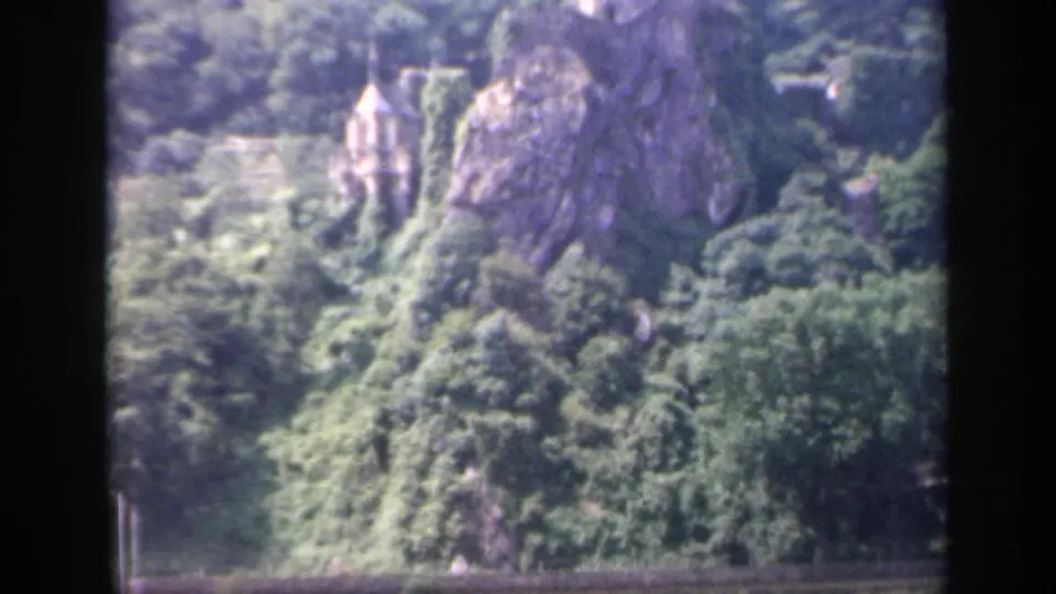End frame of the 1949 Ireland 8mm pan shows the lower rock, dense trees, and a small pointed-roof building beneath the castle site.