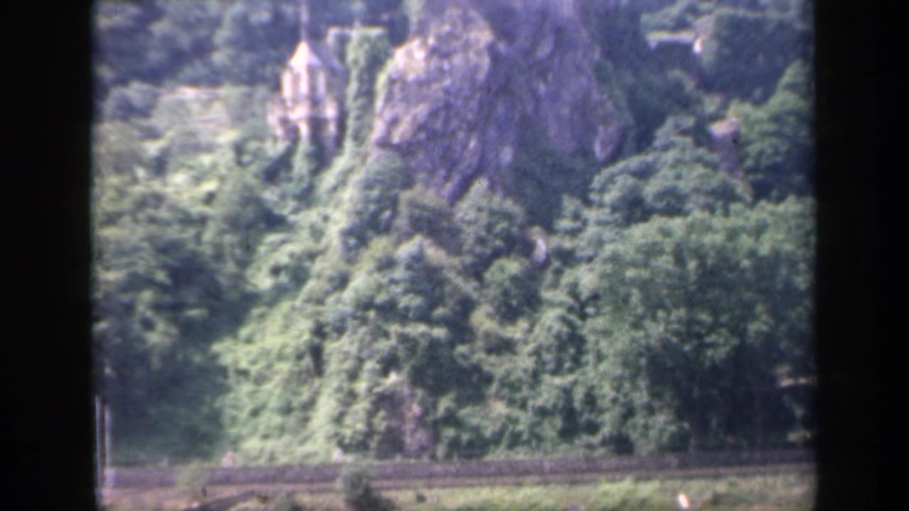 1949 Ireland 8mm frame showing a distant ivy-covered stone structure and wooded hillside through dark window-like framing.