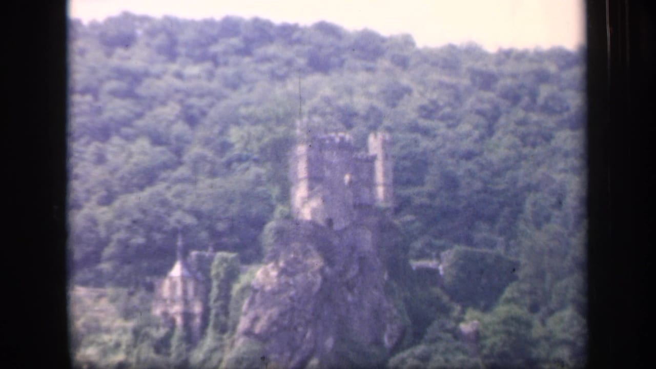 Castle-like stone structure on a forested hill with dark framing at the sides.