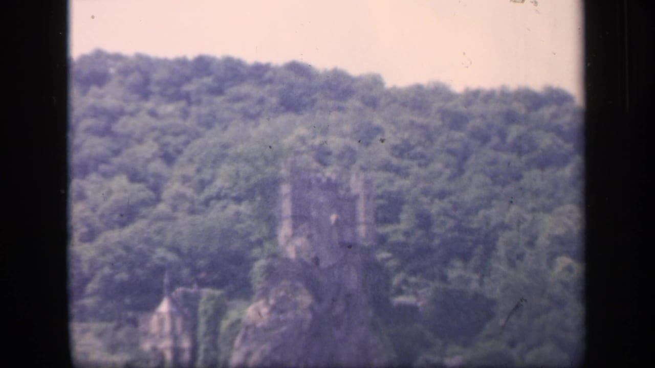 Distant stone castle ruin on a wooded hillside seen through dark window framing.