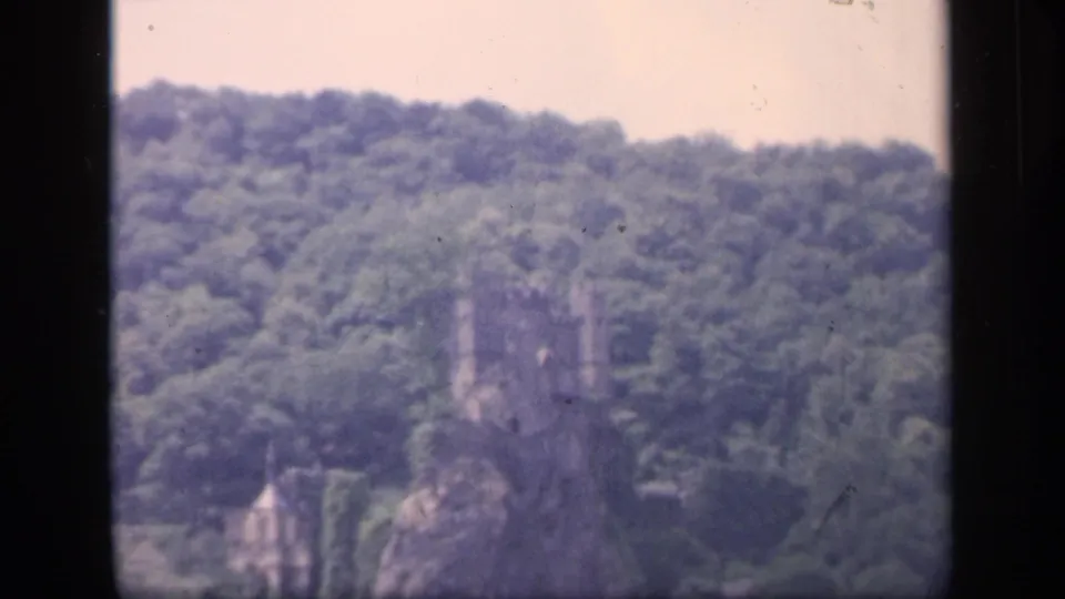 1949 Ireland 8mm frame showing a distant castle ruin among green trees, viewed through a dark window frame.