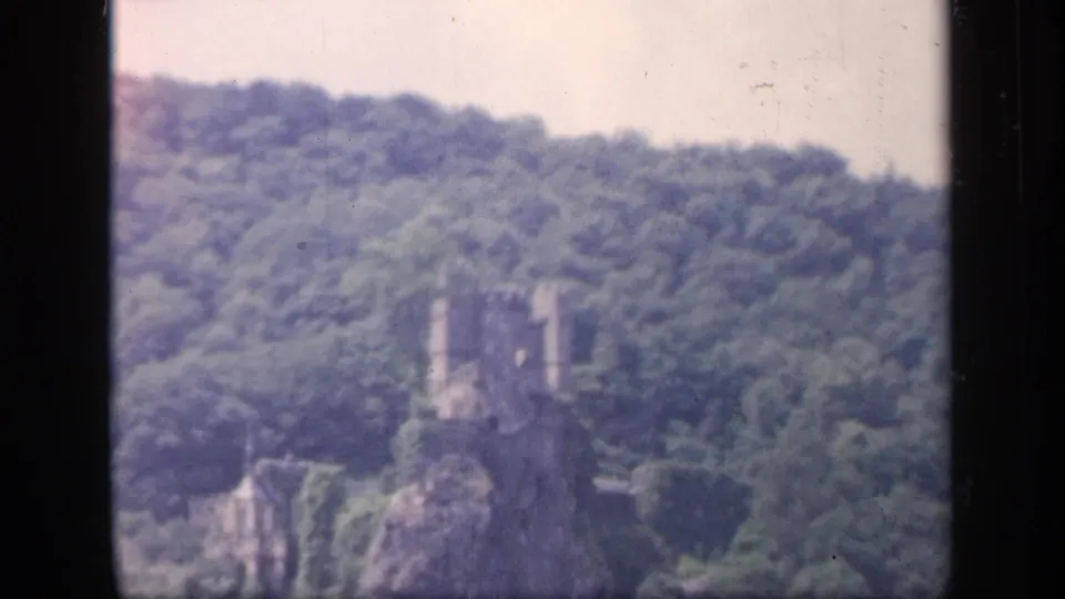 A 1949 Ireland 8mm frame shows the distant ruin and wooded slope, softened by home-movie focus and film wear.