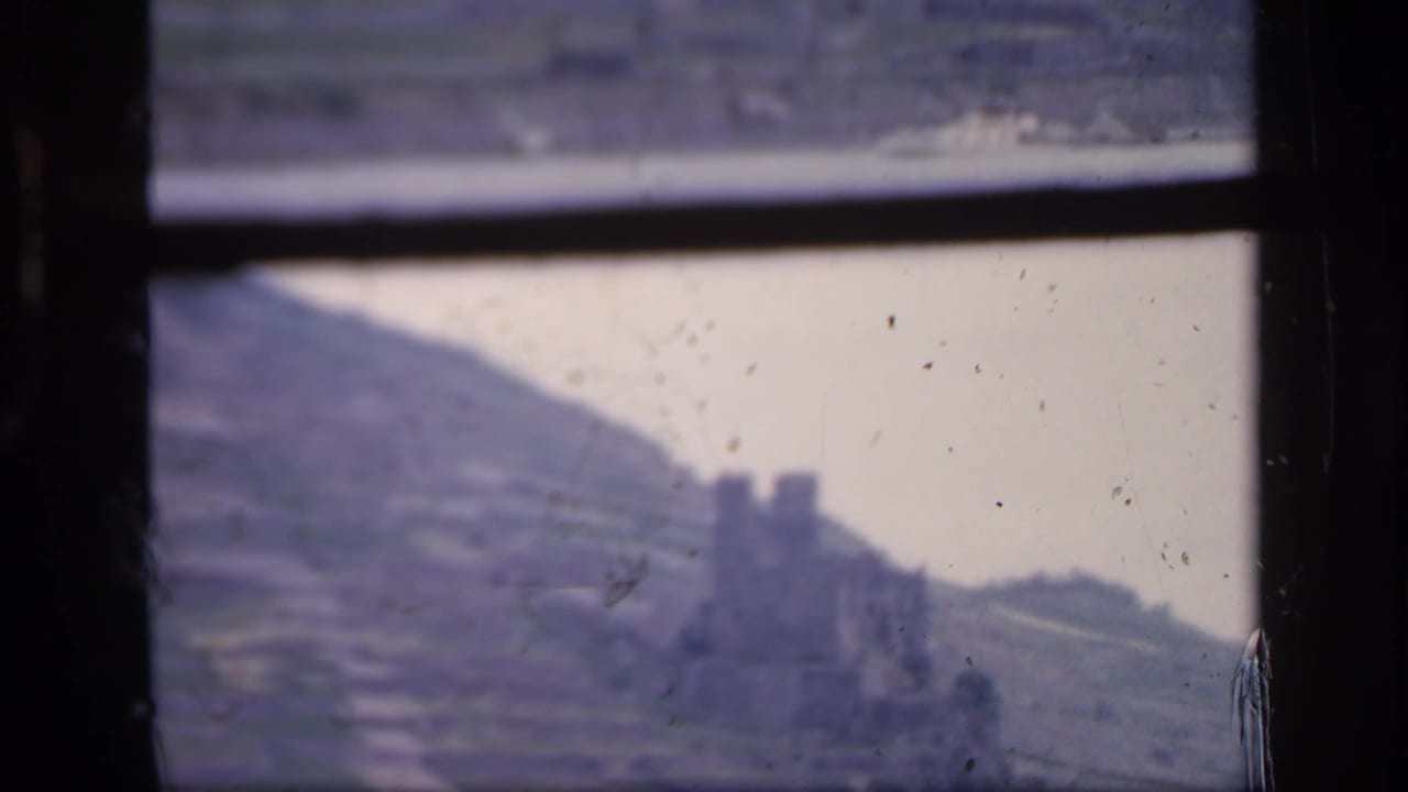 Ireland, 1949: a soft 8mm view of a castle-like ruin on a terraced hillside, partly obscured by window mullions and film wear.