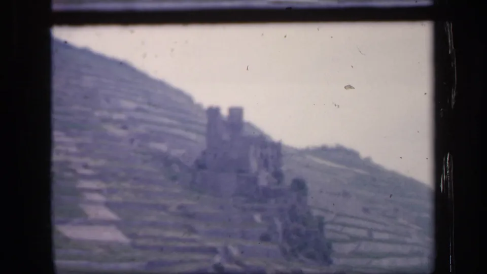 A 1949 Irish home-movie frame shows a hillside ruin and layered fields through a window, with muted color and visible 8mm film texture.