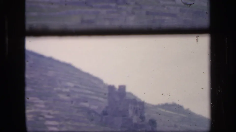 The final 1949 Ireland frame holds on the castle-like ruin and terraced hillside, seen through dark window bars with scratches and dust visible.